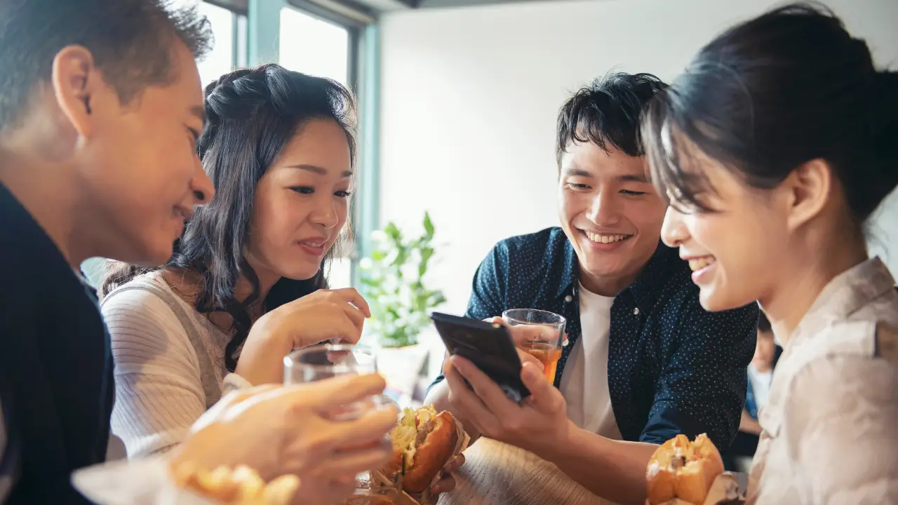 Colaboradores fazendo uma refeição e consultando o saldo do cartão de alimentação no celular.