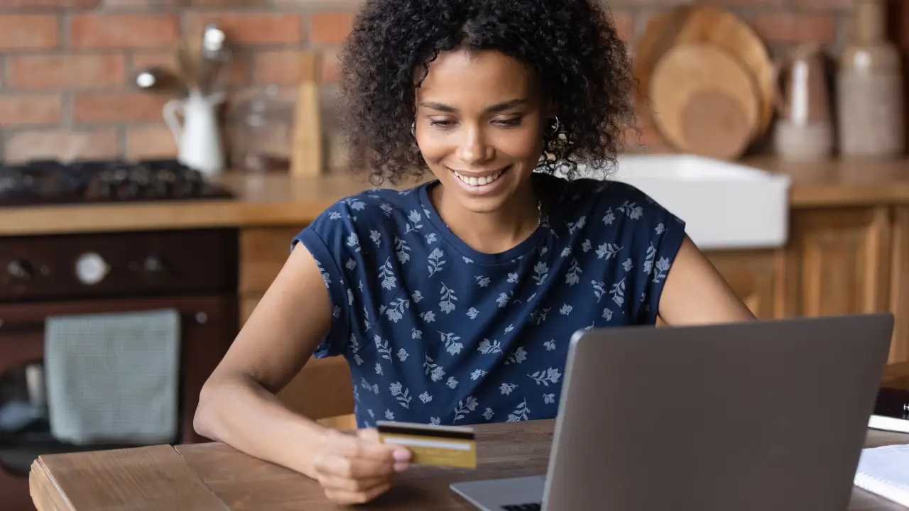 Mulher sentada em frente ao computador, olhando para o seu cartão multibenefícios.